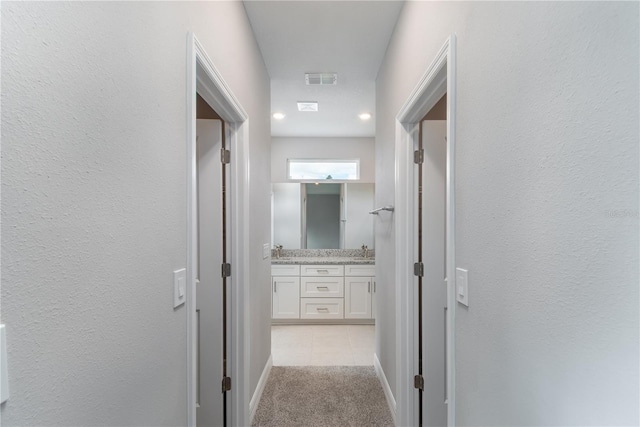 hall with a textured wall, light colored carpet, a sink, and baseboards