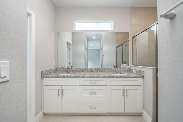 full bathroom with double vanity, a shower stall, baseboards, and a sink