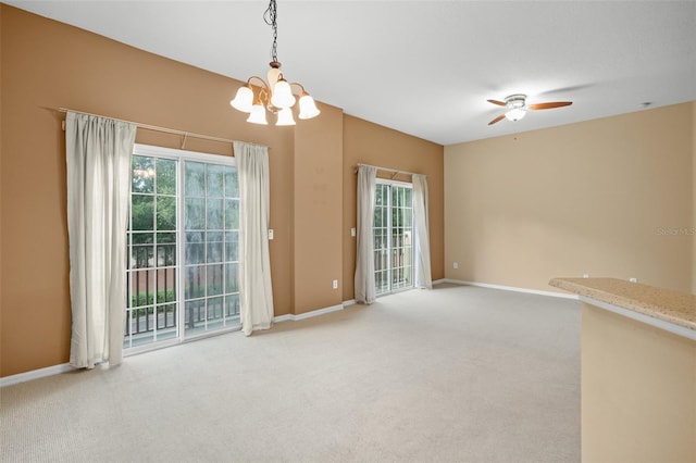 carpeted spare room featuring ceiling fan with notable chandelier