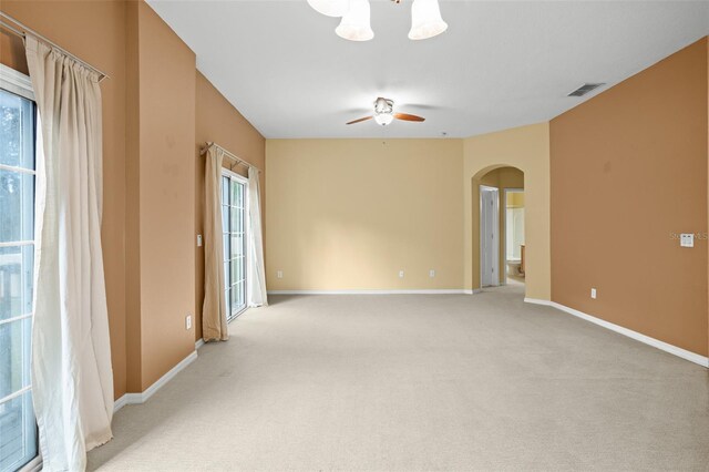 carpeted spare room featuring a wealth of natural light and ceiling fan with notable chandelier