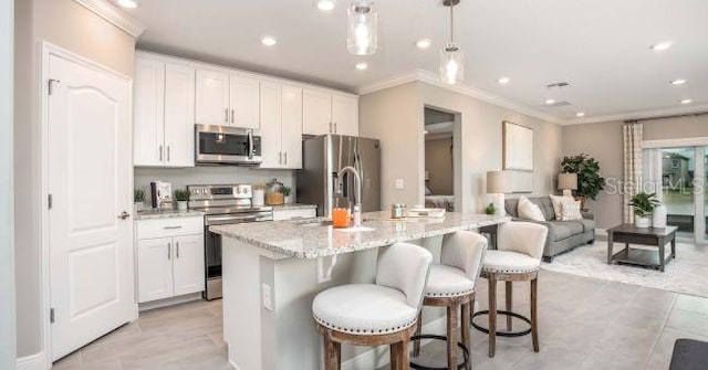 kitchen with pendant lighting, appliances with stainless steel finishes, white cabinetry, and an island with sink