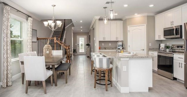 kitchen featuring white cabinetry, hanging light fixtures, stainless steel appliances, and a center island with sink