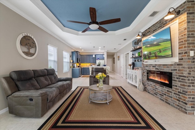 living room with a brick fireplace, light tile patterned floors, ornamental molding, and a tray ceiling