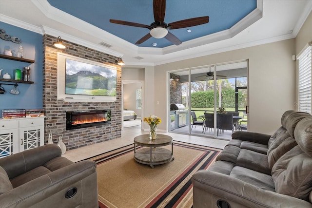 tiled living room featuring plenty of natural light, ornamental molding, a fireplace, and a tray ceiling