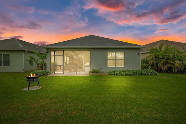 back house at dusk featuring a sunroom, an outdoor fire pit, and a lawn