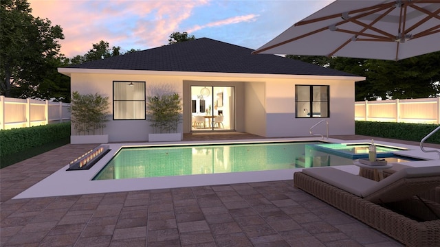 pool at dusk with a patio and an in ground hot tub