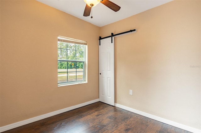 empty room featuring dark hardwood / wood-style flooring, a barn door, and ceiling fan