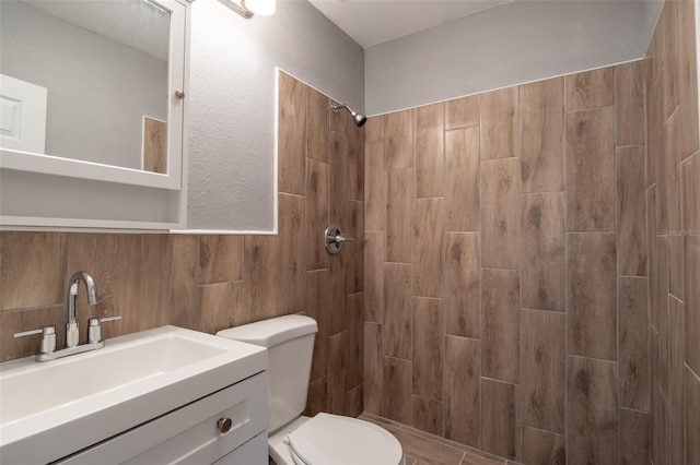 bathroom featuring wood walls, a tile shower, vanity, and toilet