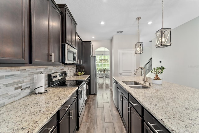 kitchen featuring hanging light fixtures, light wood-type flooring, stainless steel appliances, sink, and light stone counters