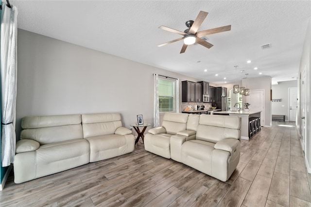 living room featuring ceiling fan, a textured ceiling, and light hardwood / wood-style flooring