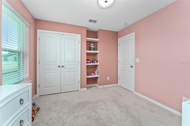 unfurnished bedroom featuring a textured ceiling, light colored carpet, and a closet