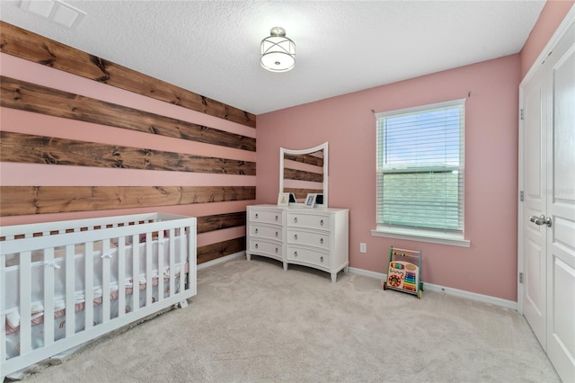 carpeted bedroom with a nursery area, a textured ceiling, and a closet