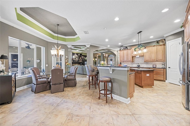 kitchen featuring stainless steel refrigerator, a center island, decorative light fixtures, a tray ceiling, and a kitchen bar