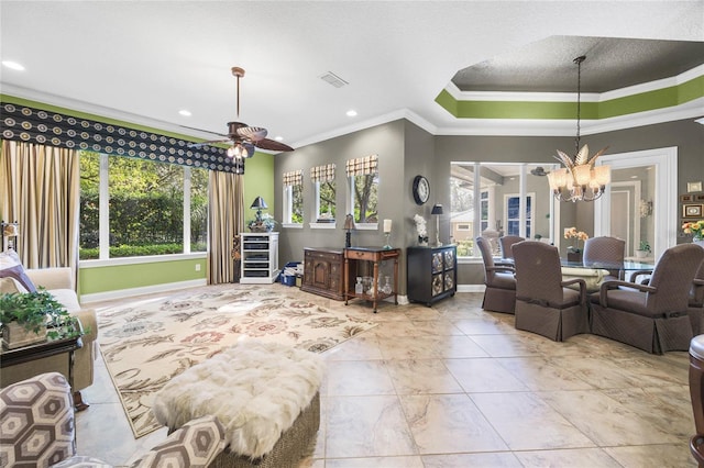 living room featuring ceiling fan with notable chandelier, a tray ceiling, and crown molding