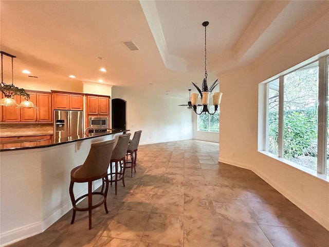 kitchen with appliances with stainless steel finishes, a kitchen breakfast bar, a tray ceiling, decorative light fixtures, and a chandelier