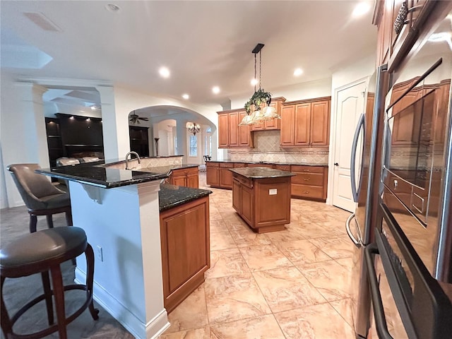 kitchen with a center island, tasteful backsplash, kitchen peninsula, dark stone countertops, and decorative light fixtures