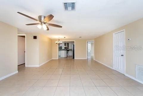 tiled spare room with ceiling fan with notable chandelier