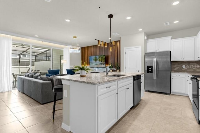 kitchen featuring an island with sink, hanging light fixtures, stainless steel appliances, sink, and white cabinets