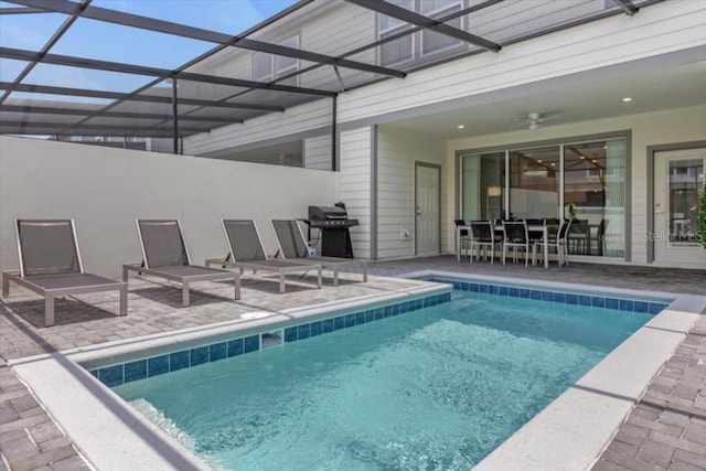 view of pool with area for grilling, a patio, glass enclosure, and ceiling fan