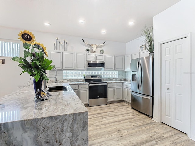 kitchen featuring tasteful backsplash, light stone counters, stainless steel appliances, sink, and light hardwood / wood-style flooring