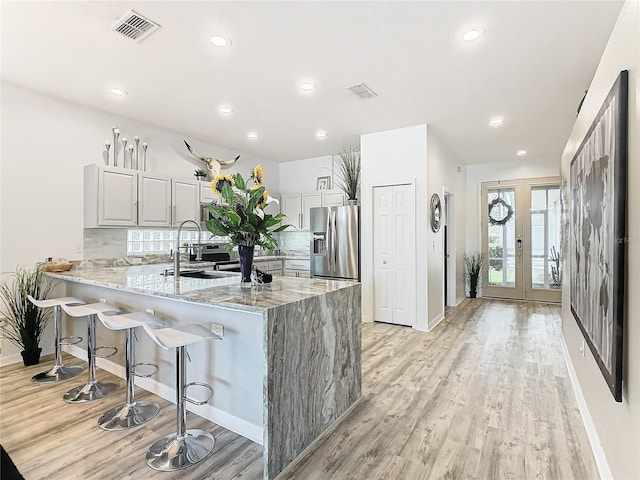 kitchen with decorative backsplash, stainless steel fridge, light stone countertops, light hardwood / wood-style floors, and kitchen peninsula