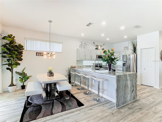 kitchen featuring kitchen peninsula, light stone counters, decorative light fixtures, a chandelier, and stainless steel fridge with ice dispenser