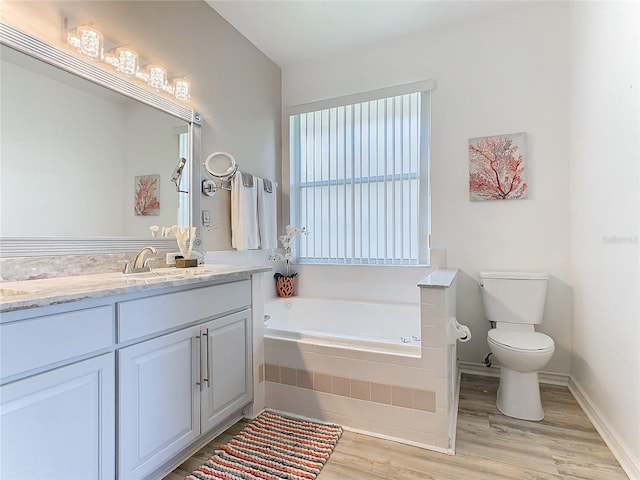 bathroom with a relaxing tiled tub, toilet, wood-type flooring, and vanity