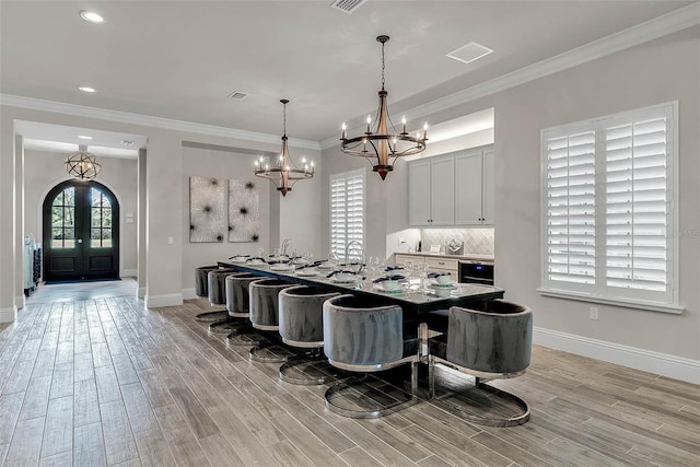 kitchen featuring french doors, light wood-type flooring, tasteful backsplash, ornamental molding, and an island with sink