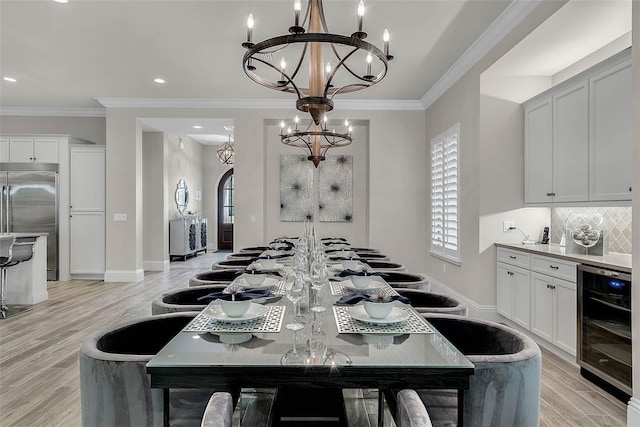 dining space featuring light hardwood / wood-style flooring, an inviting chandelier, beverage cooler, and ornamental molding