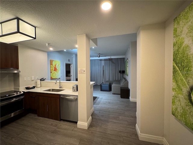 kitchen with a textured ceiling, ventilation hood, stainless steel appliances, dark wood-type flooring, and sink