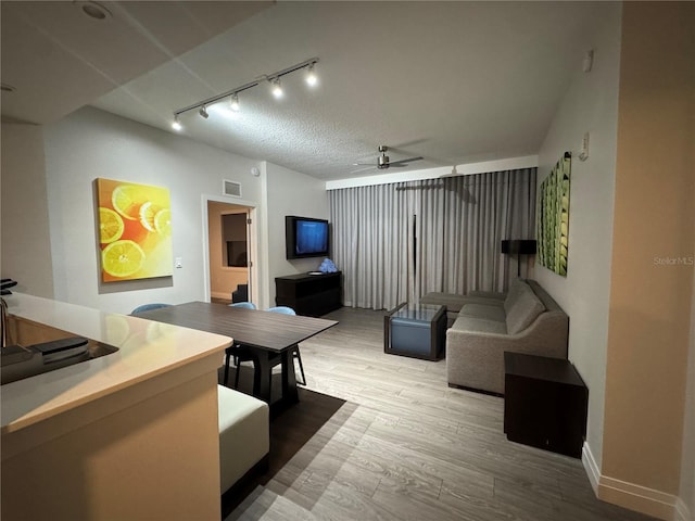 living room with ceiling fan, rail lighting, wood-type flooring, and a textured ceiling