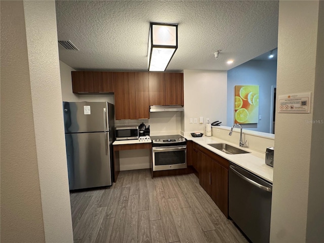 kitchen with sink, light wood-type flooring, a textured ceiling, and appliances with stainless steel finishes