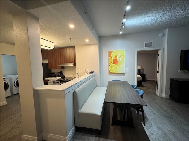 kitchen with washer and clothes dryer, dark wood-type flooring, a textured ceiling, kitchen peninsula, and a breakfast bar area