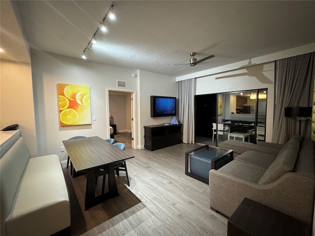 living room with rail lighting, ceiling fan, a textured ceiling, and light hardwood / wood-style flooring