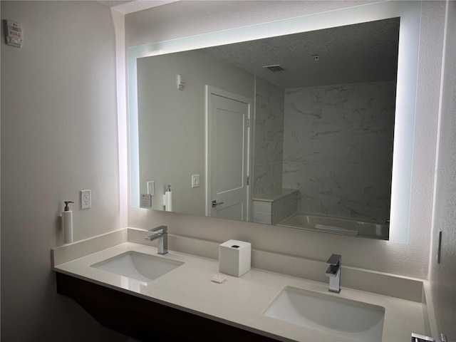 bathroom featuring vanity, a textured ceiling, and tiled shower / bath