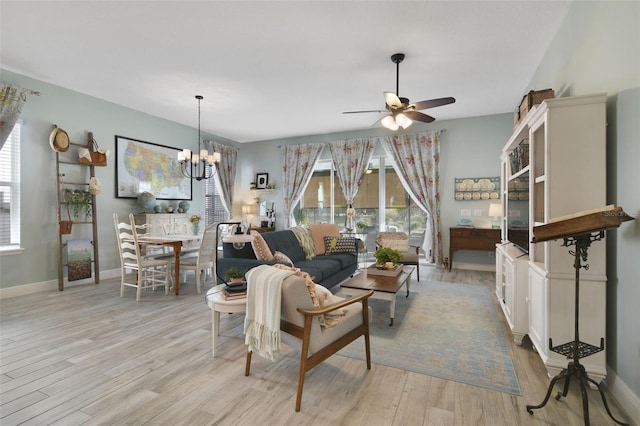 living room with a wealth of natural light, light hardwood / wood-style flooring, and ceiling fan with notable chandelier