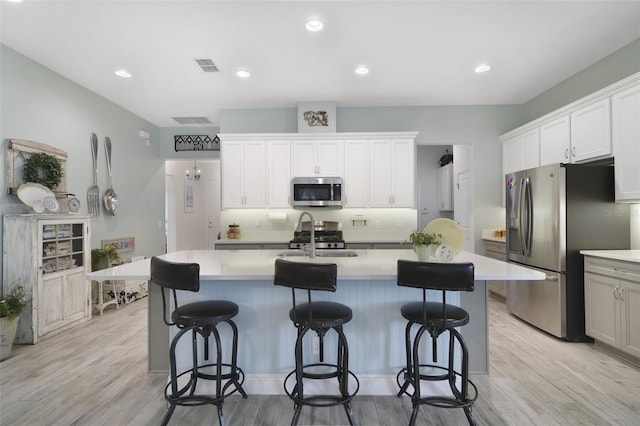 kitchen featuring a center island with sink, white cabinetry, light wood-type flooring, stainless steel appliances, and sink