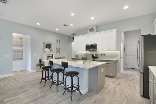 kitchen featuring an island with sink, stainless steel appliances, sink, light wood-type flooring, and white cabinets