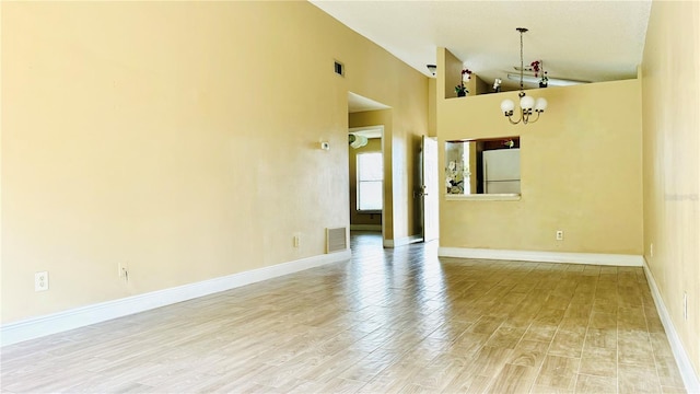 empty room with hardwood / wood-style floors, a notable chandelier, and high vaulted ceiling