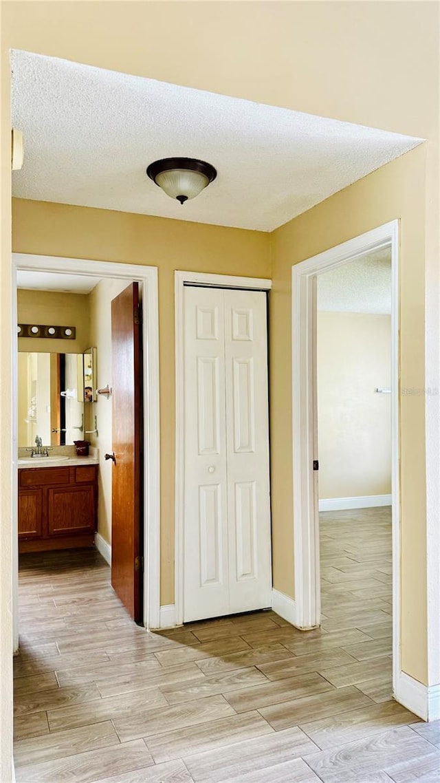 hallway featuring sink, light hardwood / wood-style flooring, and a textured ceiling