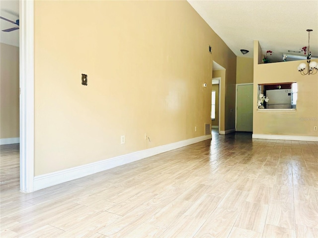 unfurnished living room with light hardwood / wood-style floors, ceiling fan with notable chandelier, and high vaulted ceiling