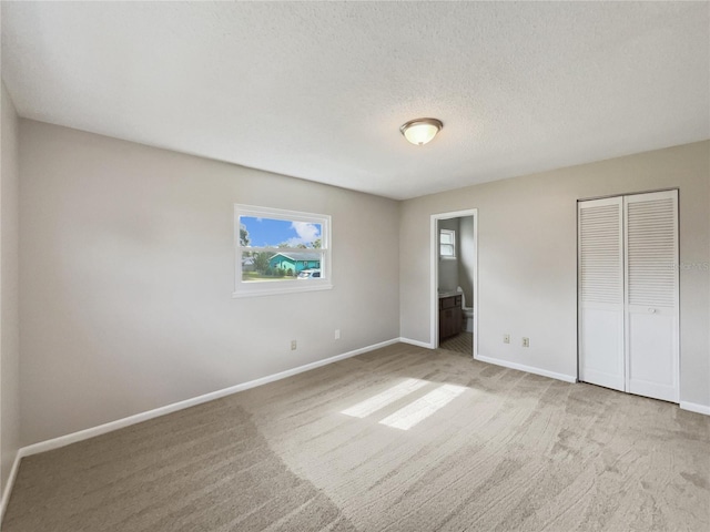 unfurnished bedroom featuring a textured ceiling, light colored carpet, and ensuite bath