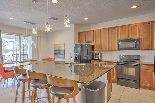 kitchen with black appliances, a textured ceiling, pendant lighting, sink, and a kitchen island with sink