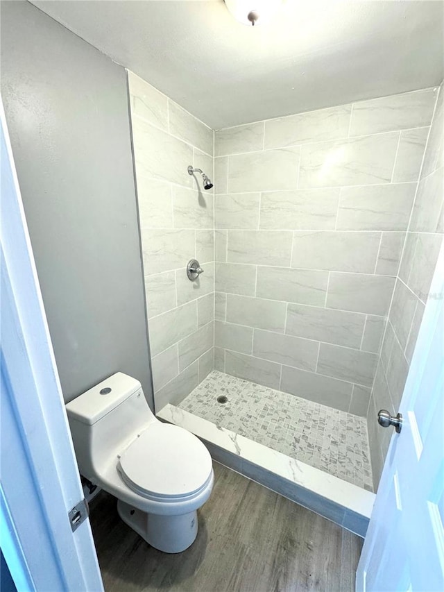 bathroom with toilet, tiled shower, and hardwood / wood-style floors