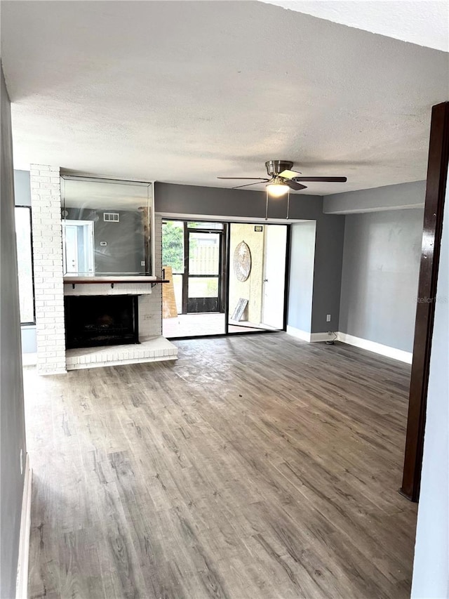 unfurnished living room with a brick fireplace, a textured ceiling, hardwood / wood-style flooring, and ceiling fan