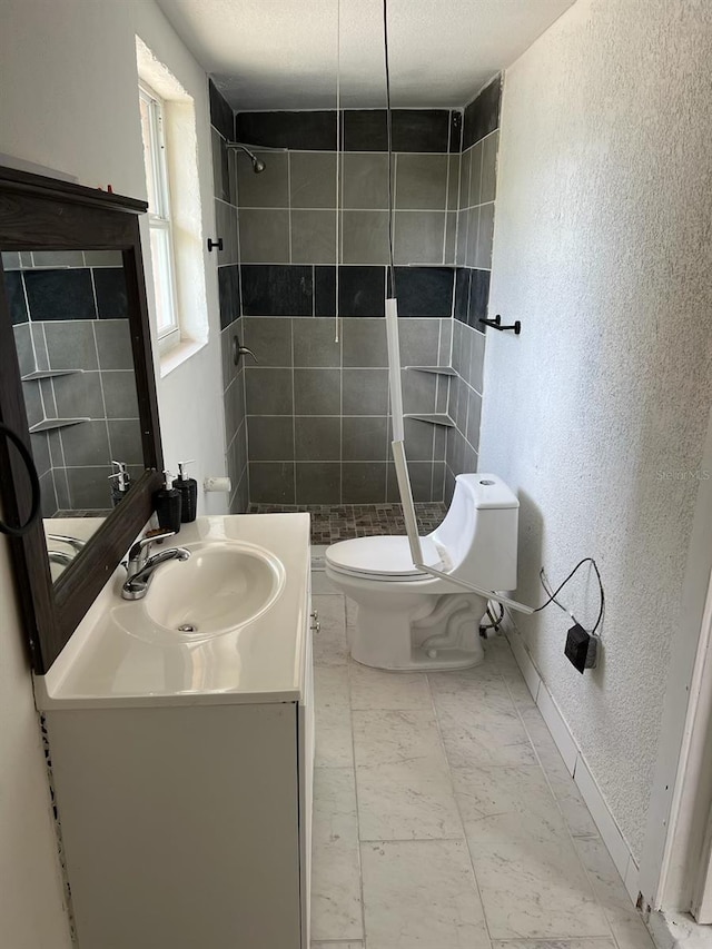 bathroom featuring a tile shower, vanity, a textured ceiling, and toilet