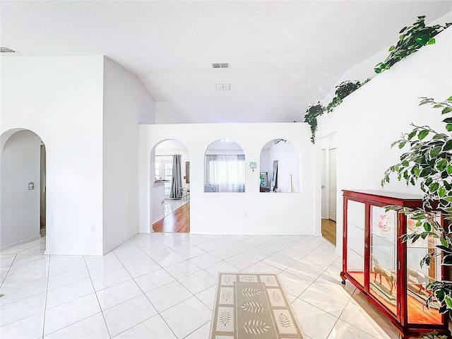 interior space featuring lofted ceiling, light tile patterned flooring, and a textured ceiling