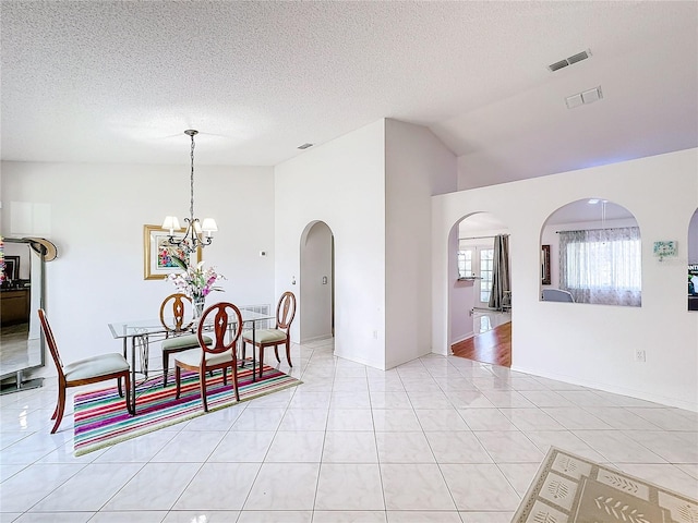 dining room featuring lofted ceiling, a textured ceiling, an inviting chandelier, and light tile patterned floors