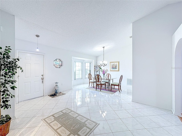 tiled entrance foyer with a notable chandelier, a textured ceiling, and vaulted ceiling