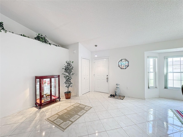 foyer entrance featuring vaulted ceiling, a textured ceiling, and light tile patterned floors